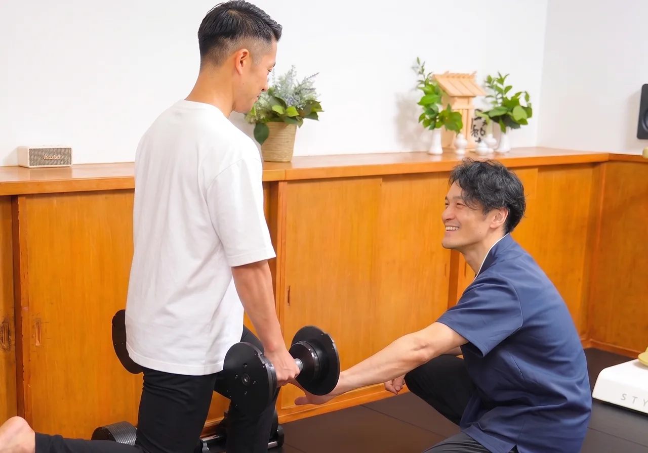ダンベルを持つ利用者にスタッフが姿勢を確認しながら声をかけている様子
