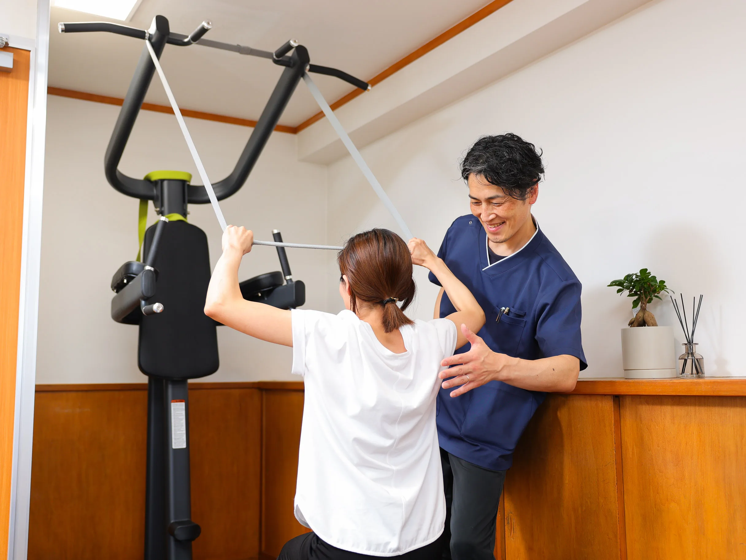 トレーニング機器を使う利用者にスタッフが肩まわりの動きを確認している様子