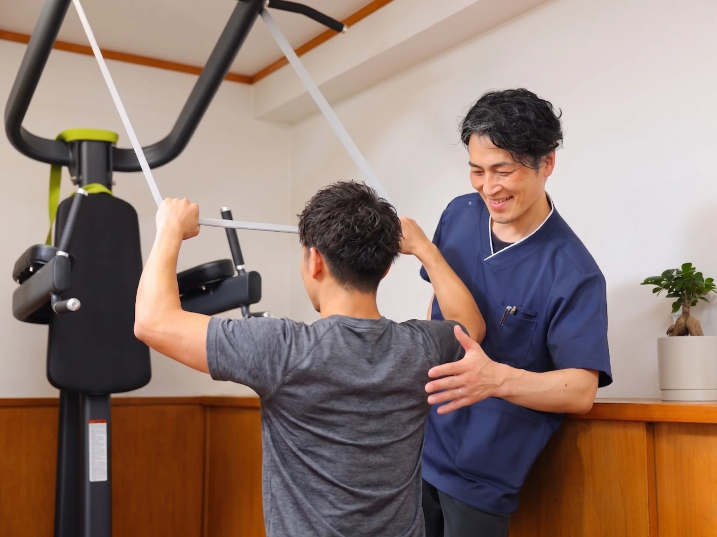 ケーブルマシンを使って利用者が体幹トレーニングを行い、トレーナーがフォームを横から見ている様子